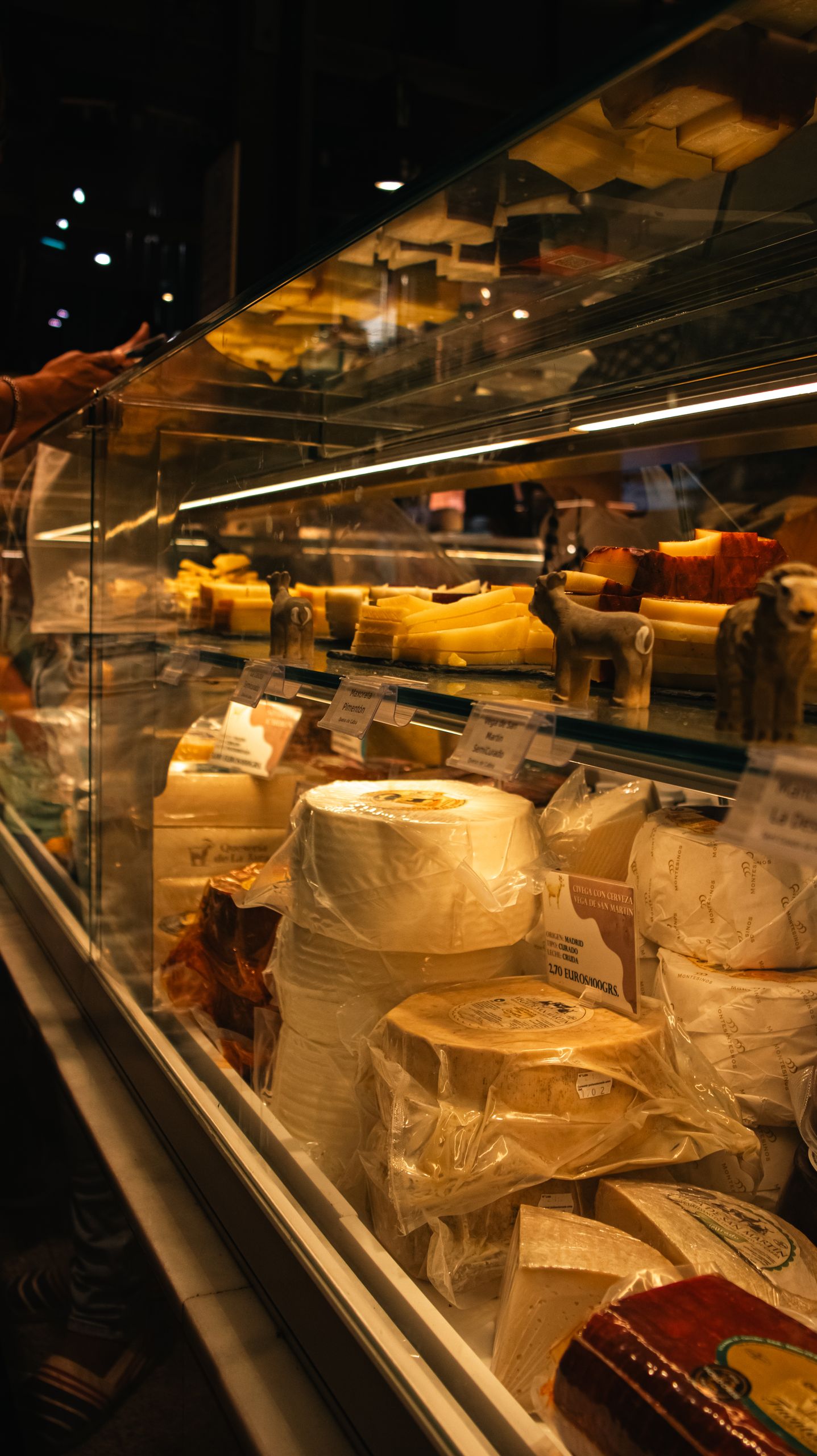 Showcases various cheeses inside a Madrid market's glass display case.